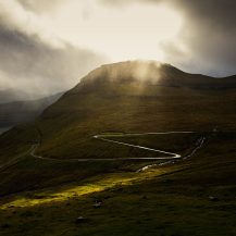 <p>A momentary spotlight of sunshine illuminates the winding road out of Funningur.</p>