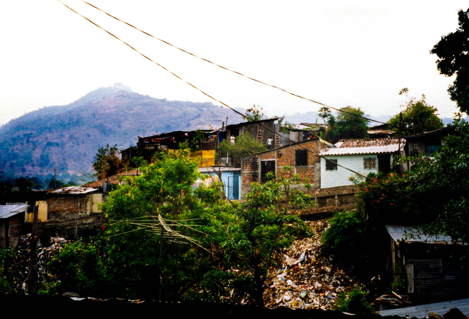 <p>A cluster of makeshift homes on the outskirts of San Salvador. Such homes represent years of effort by their inhabitants, but often these neighbourhoods lack essential services like plumbing, refuse collection, and official recognition of the residents' title to their land. These districts are peripheries not only in the geographical sense, but also in terms of political and economic attention.</p>
